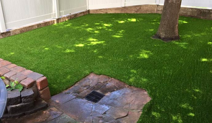 A stone patio drain inset into an artificial grass backyard