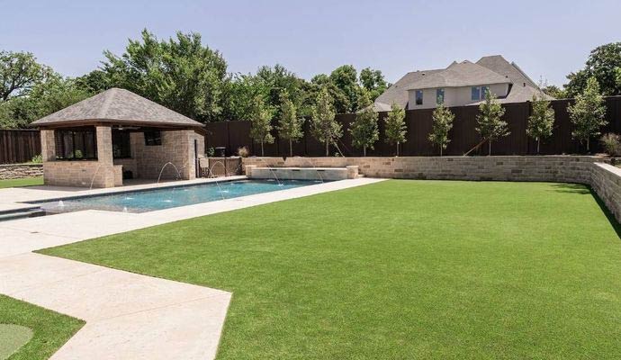 An outdoor residential swimming pool area with synthetic grass lawn