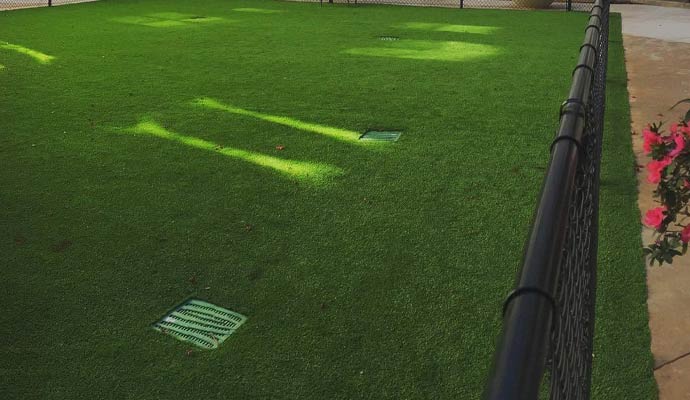 An outdoor synthetic grass play area featuring multiple basin drains