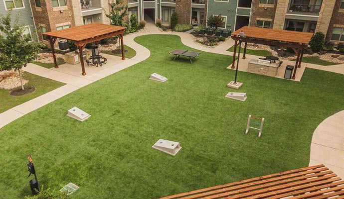 Apartment courtyard with artificial turf, cornhole, and grilling stations.