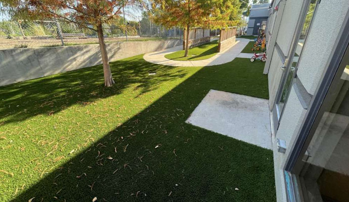 Fallen leaves and twigs scattered across an artificial turf lawn beside a building