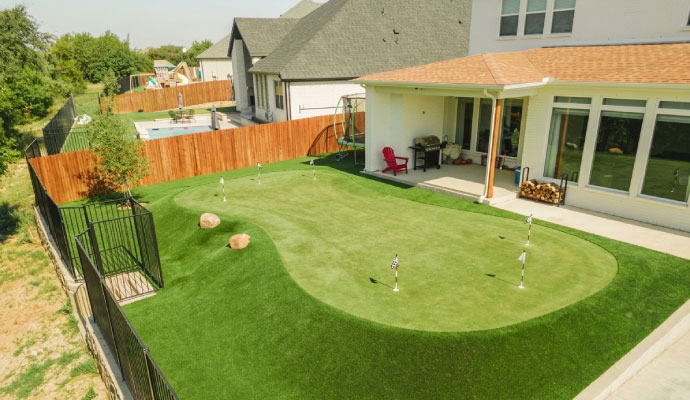 Residential backyard with artificial turf putting green and landscaped outdoor recreation area beside modern home