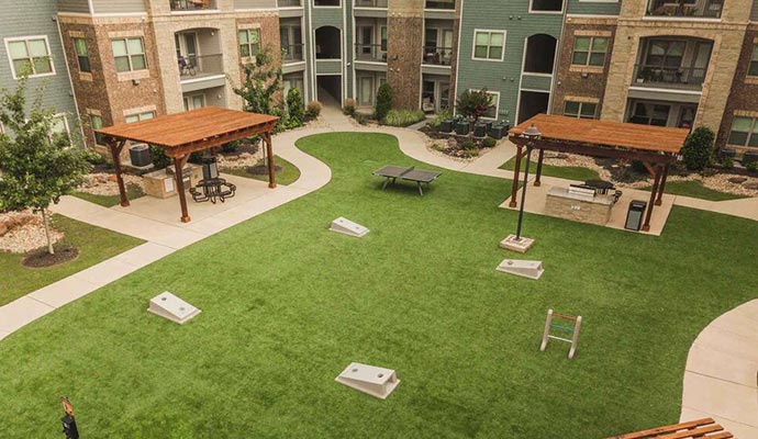 Apartment courtyard with artificial turf, cornhole, and grilling stations.