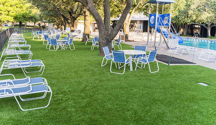 Poolside synthetic turf lawn with lounge chairs tables and shade trees at a country club