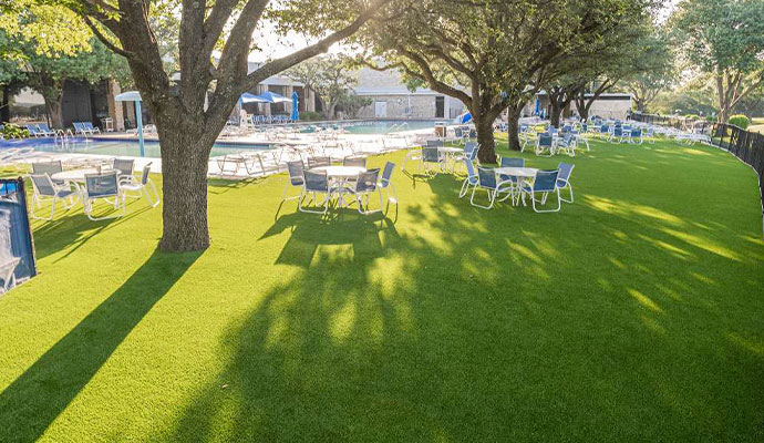 Sprawling synthetic turf lawn with outdoor dining tables under shade trees at a country club
