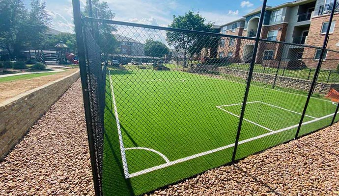 Fenced outdoor synthetic turf sports field in apartment community