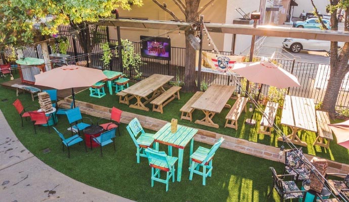 Outdoor restaurant patio with artificial turf, picnic tables, and lawn games.
