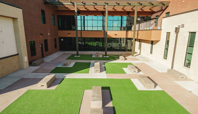 Enclosed school courtyard with artificial turf patches, concrete benches, and overhead pergola