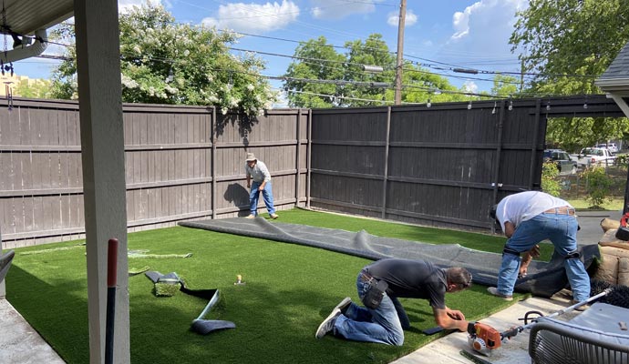 Crew installing artificial turf in a backyard.