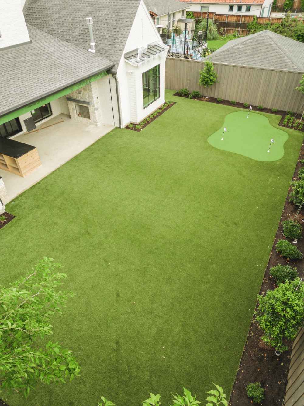 Aerial view of a modern backyard with a putting green near a house with an outdoor fireplace.