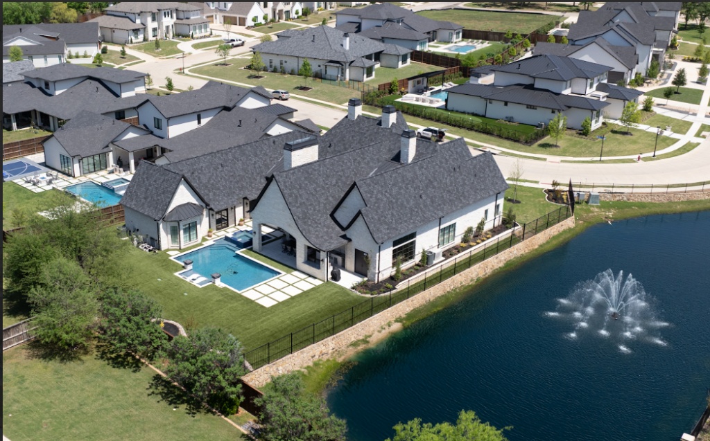 A stunning aerial view of a lakeside home with a complete backyard transformation, featuring a low-maintenance artificial turf lawn and a modern pool with turf strips for a clean, cohesive outdoor living space.