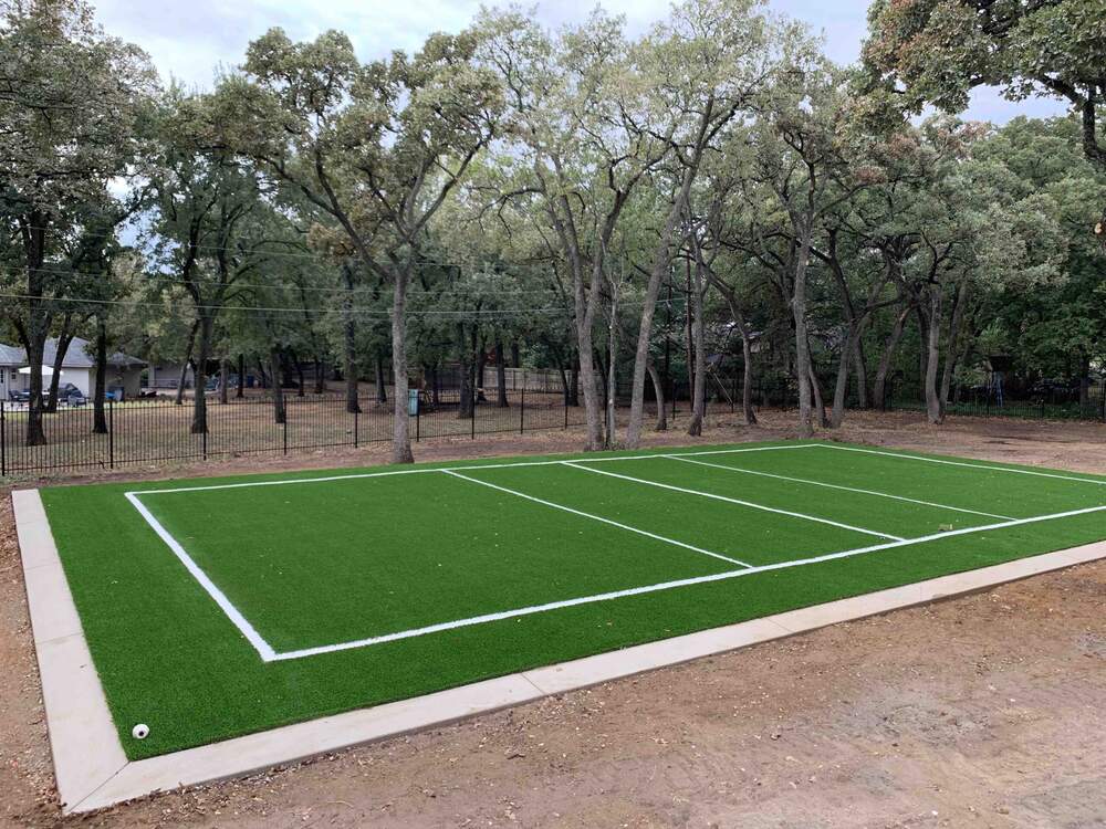 Custom artificial turf volleyball court installed in a residential backyard, designed for year-round family and friends' recreational activities, blending with natural trees and fencing.