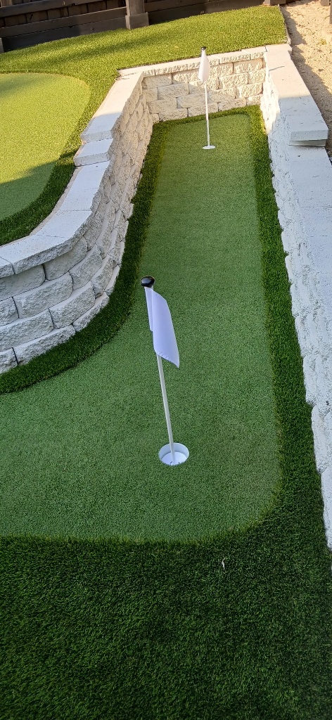Custom residential putting green installation featuring high-performance synthetic turf installation with a clean, tiered design. This backyard golf green offers a realistic, low-maintenance pool decking amenity, completing the elegant outdoor retreat with year-round recreational value and premium synthetic turf.