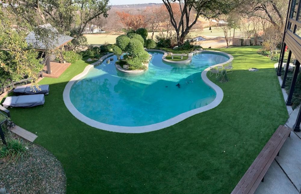 Expansive view of artificial grass decking around a custom backyard pool, creating a maintenance-free and immaculate outdoor living space. This artificial turf solution keeps the pool free from natural grass debris and enhances the aesthetic appeal.