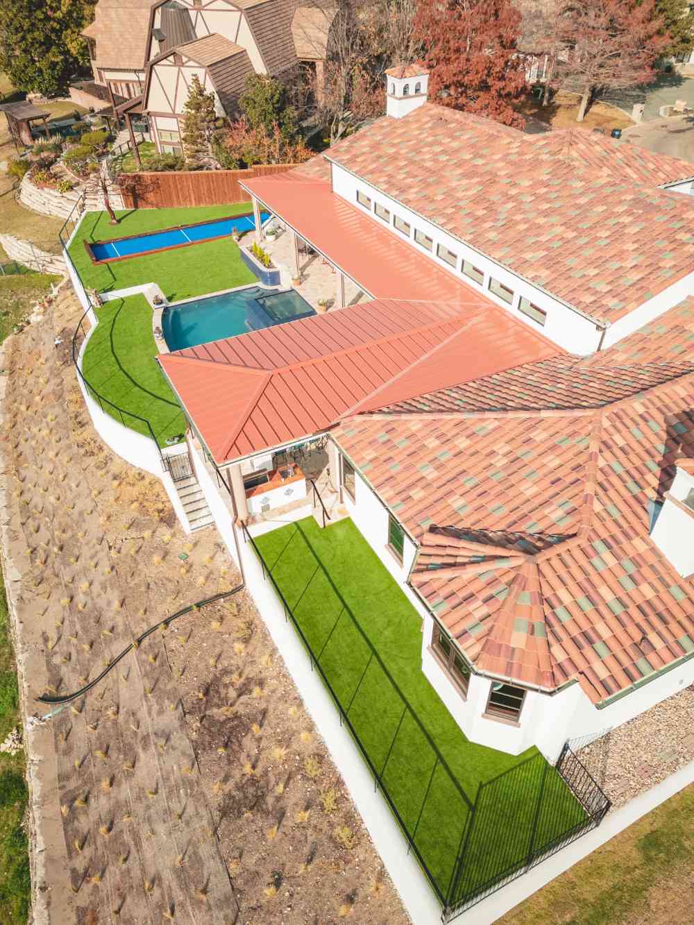 An aerial view of a luxurious backyard, showcasing a sleek artificial turf installation that includes a dedicated dog run and seamlessly wraps around a swimming pool, creating a low-maintenance, functional outdoor space.