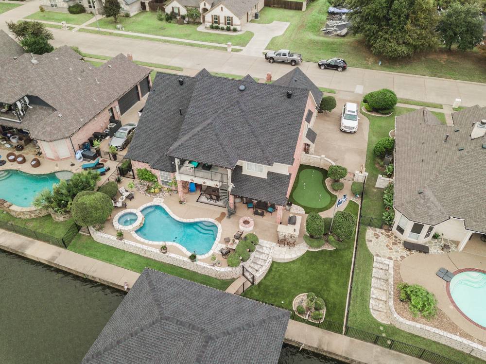 Aerial view of a luxury backyard featuring an artificial turf putting green, a swimming pool with integrated spa, and outdoor entertainment areas, showcasing a low-maintenance, green landscape.