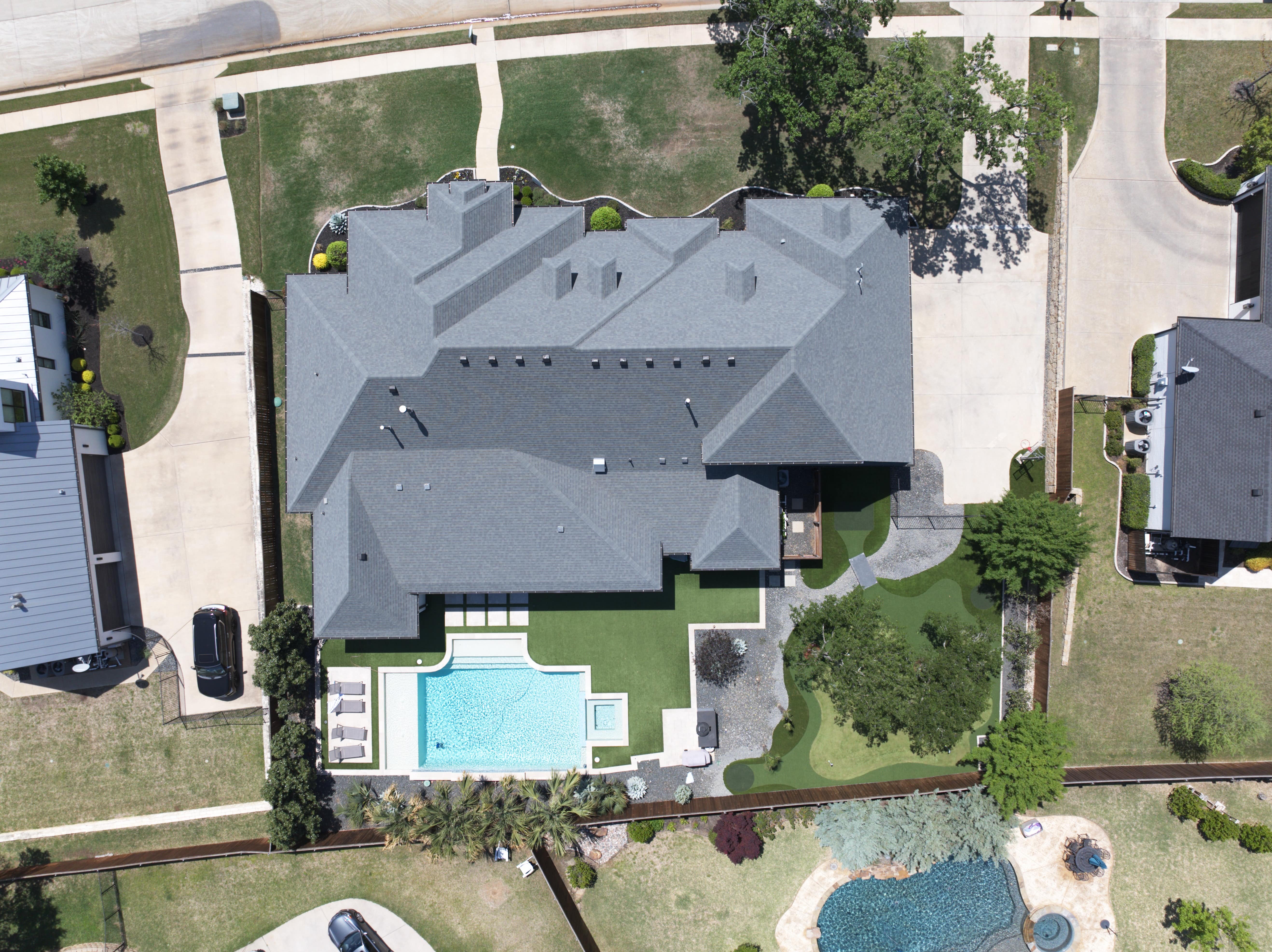Top-down aerial view of a residential neighborhood featuring houses with backyard pools, decks, and recreational areas
