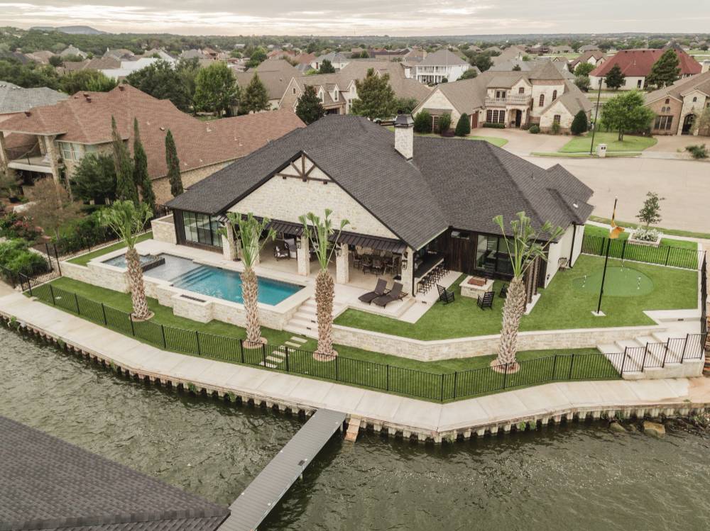 Artificial turf and synthetic grass putting green installed at a lakeside property to create a stunning, low-maintenance outdoor space with a pool and palm trees.