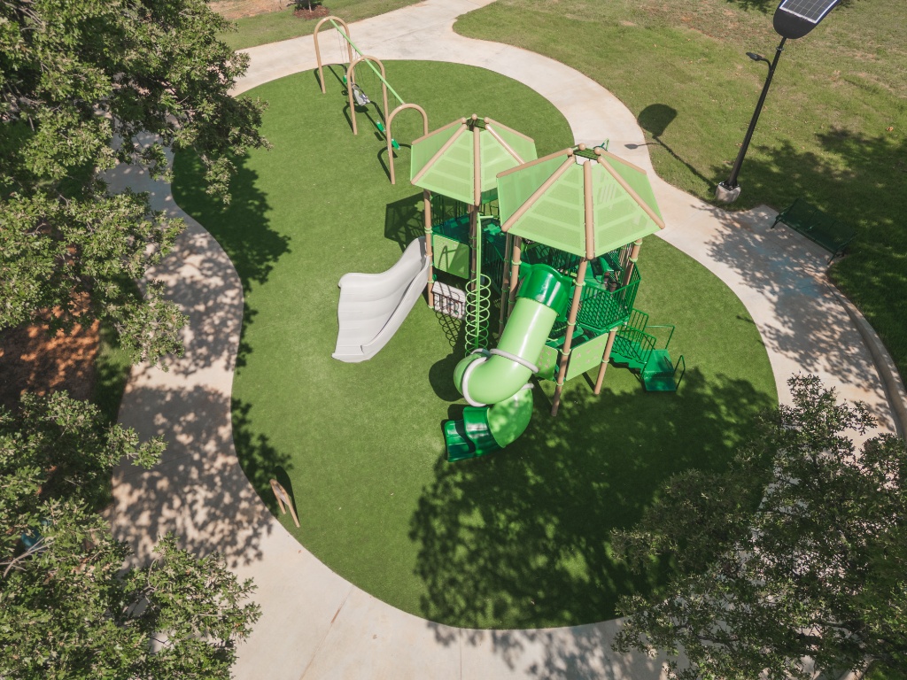 Overhead view of a successful commercial play area surfacing project for the City of Arlington, utilising durable synthetic turf for maximum safety and longevity. The safe artificial grass provides a low-maintenance park turf solution around the custom play structure and swings, creating a vibrant public playground turf for the community.