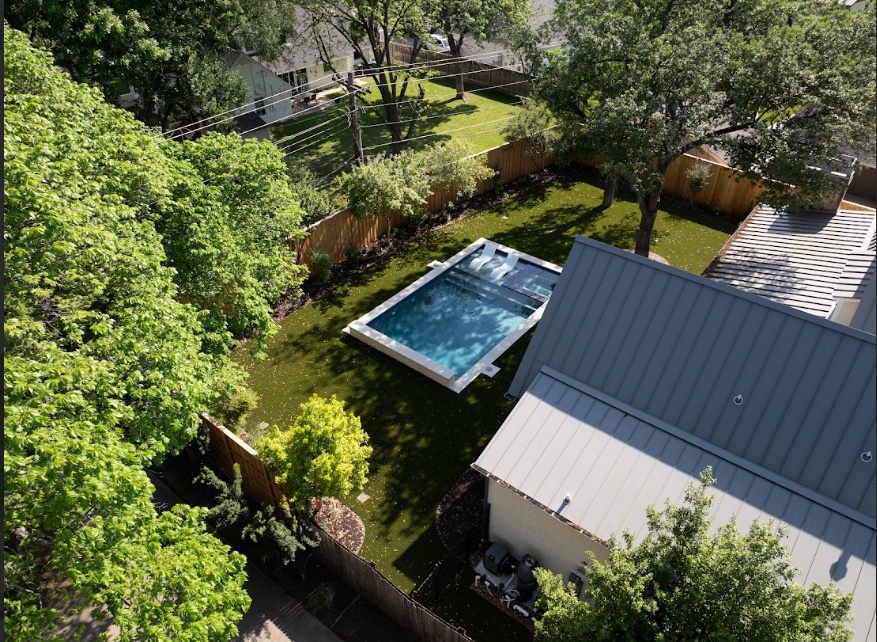 A beautiful backyard pool area surrounded by artificial turf, providing a low-maintenance, clean, and durable lawn that thrives in the shade from surrounding trees.