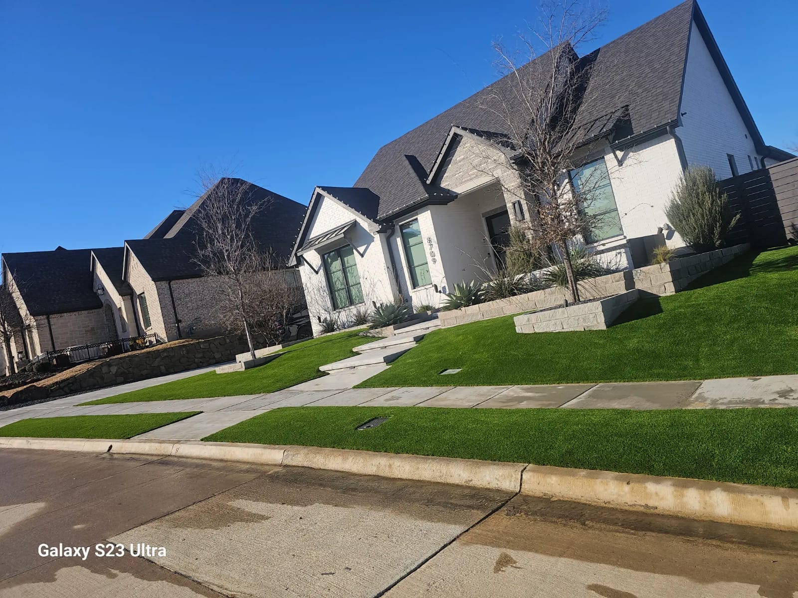 A complete front yard landscaping project with artificial turf, modern paver walkways, and tiered flower beds, providing a pristine, low-maintenance, and HOA-compliant lawn for a stunning residential property.