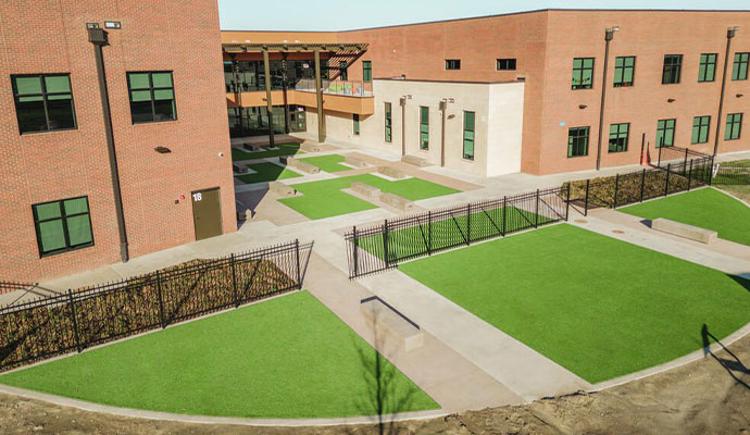 School campus courtyard featuring multi-level synthetic turf lawns, walkways, and benches