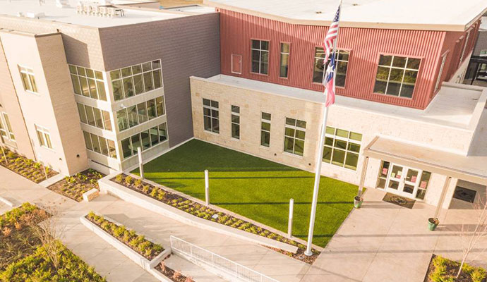 Aerial view of a school building with an artificial turf courtyard lawn and flagpole