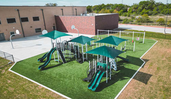 School playground structure with green synthetic safety turf and green shade canopies