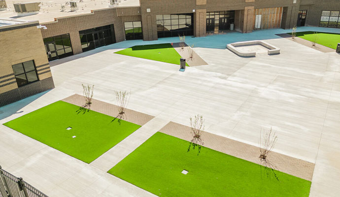 School plaza courtyard with integrated artificial turf sections and trees among concrete pavement