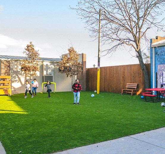 People playing soccer in an urban courtyard with artificial turf.