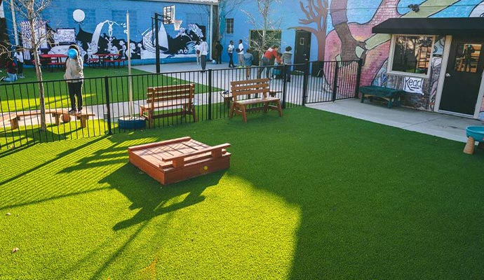 Urban play area with artificial turf, a sandbox, and colorful murals.